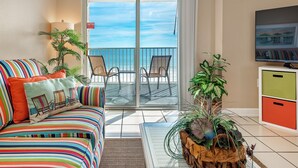 Een balkon met uitzicht op de oceaan, een gestreepte bank, twee stoelen, een televisie en een kast.