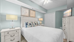A bedroom with a bed, two bedside tables, a nightstand, a dresser, a ceiling fan, and a door.