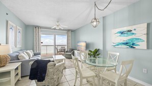 A spacious living area with a balcony, a dining table with chairs, a sofa, and a television. - Dog friendly beachfront condo with in/out pools (Gulf Shores)