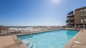 A swimming pool with clear blue water, a metal fence, and a view of the beach. - Dog friendly beachfront condo with in/out pools (Gulf Shores)