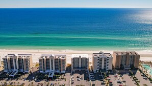 A beachfront hotel with multiple buildings, a parking lot, and a clear view of the ocean. - Beachfront condo with glass-enclosed balcony (Gulf Shores)