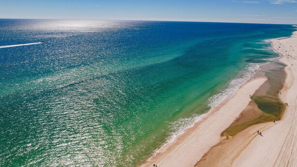 An aerial view of a beach with clear turquoise waters and a sandy shoreline. - Beachfront condo with glass-enclosed balcony (Gulf Shores)