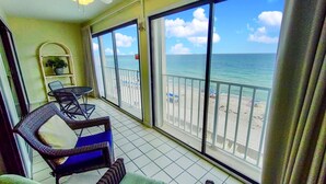 A balcony with a view of the beach, a ceiling fan, and a small table with chairs. - Beachfront condo with glass-enclosed balcony (Gulf Shores)