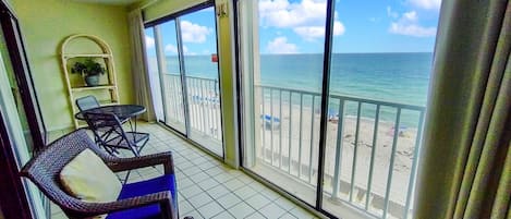 Un balcón con vista a la playa, un ventilador de techo y una mesita con sillas.