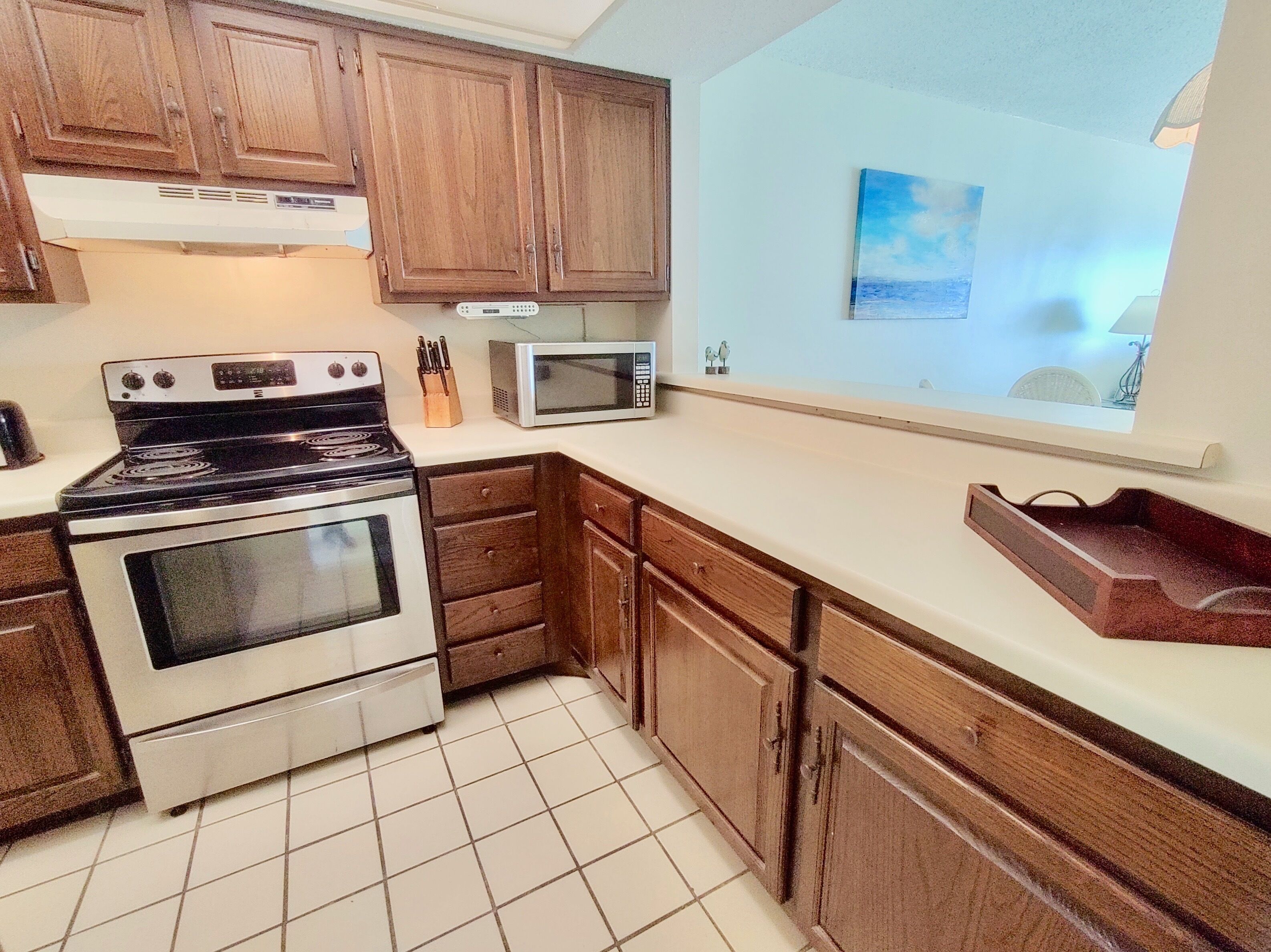 A kitchen with wooden cabinets, a stove, a microwave, and a window with a view.
