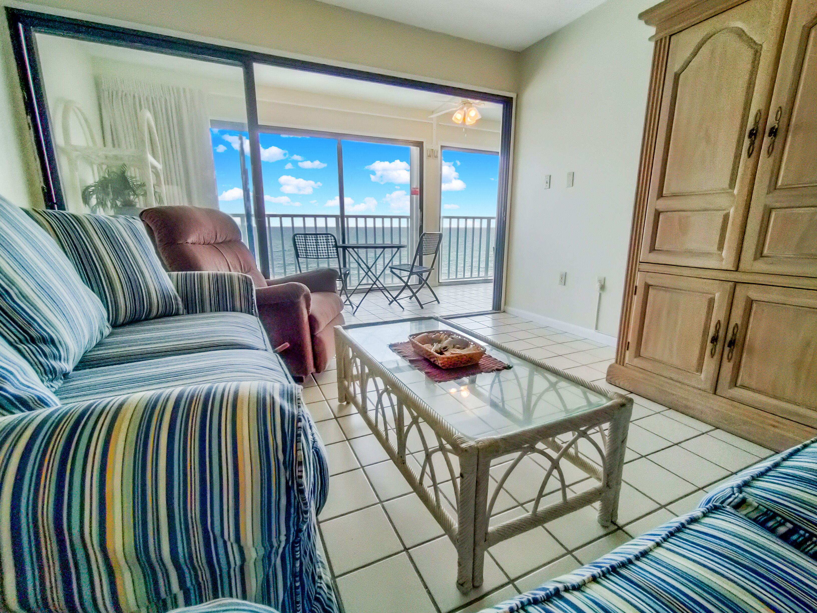 A room with a striped sofa, a glass coffee table, and a view of the sea through large windows.