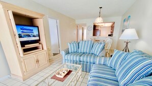 A living room with a television, striped sofa, and a dining area. - Beachfront condo with glass-enclosed balcony (Gulf Shores)