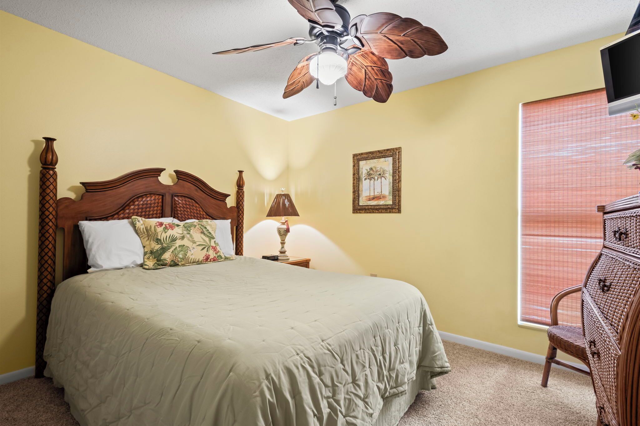 A bedroom with a bed, a ceiling fan, a nightstand, a lamp, a dresser, and a window with blinds.
