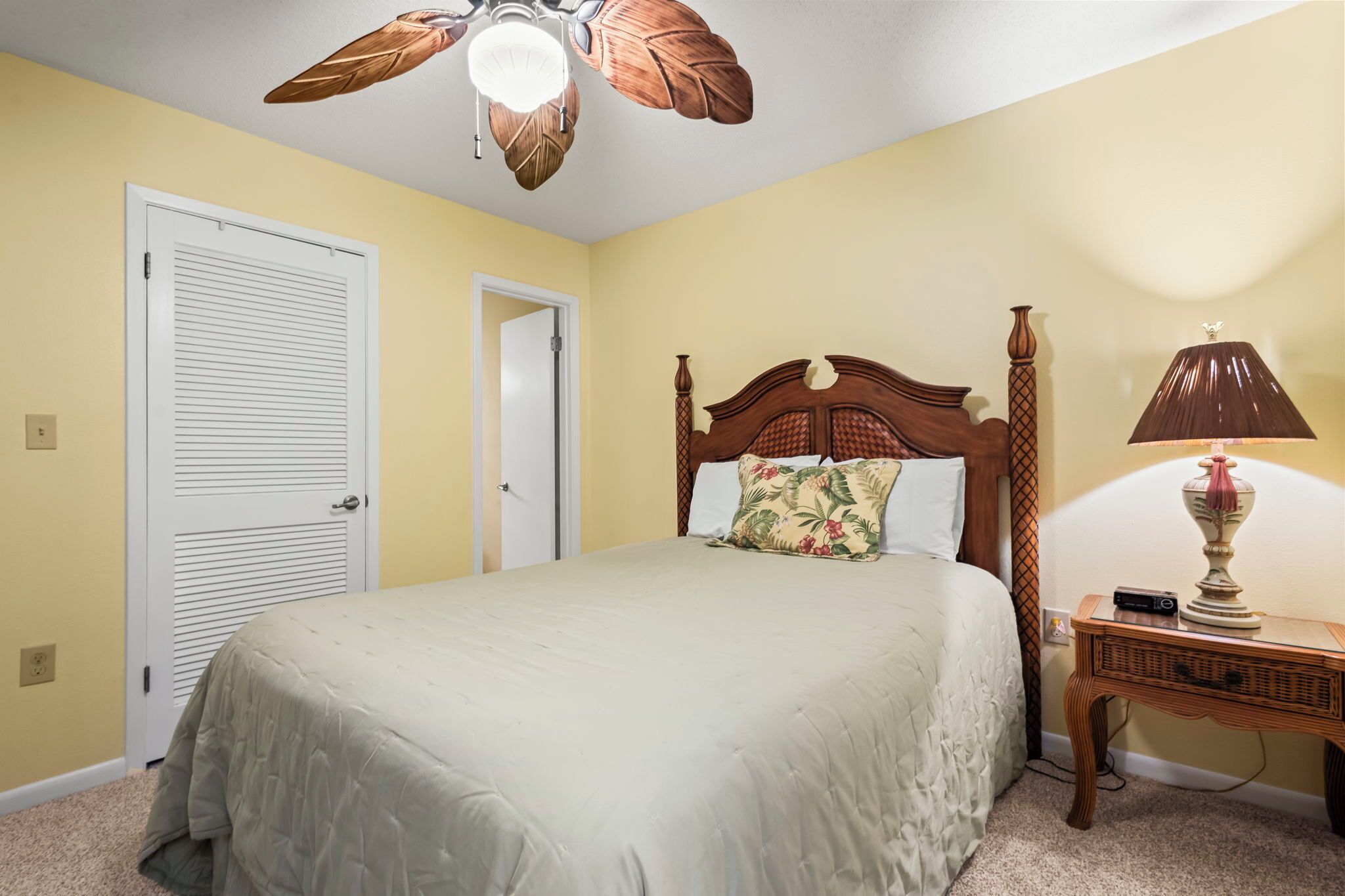 A bedroom with a bed, a ceiling fan, a nightstand, and a lamp.