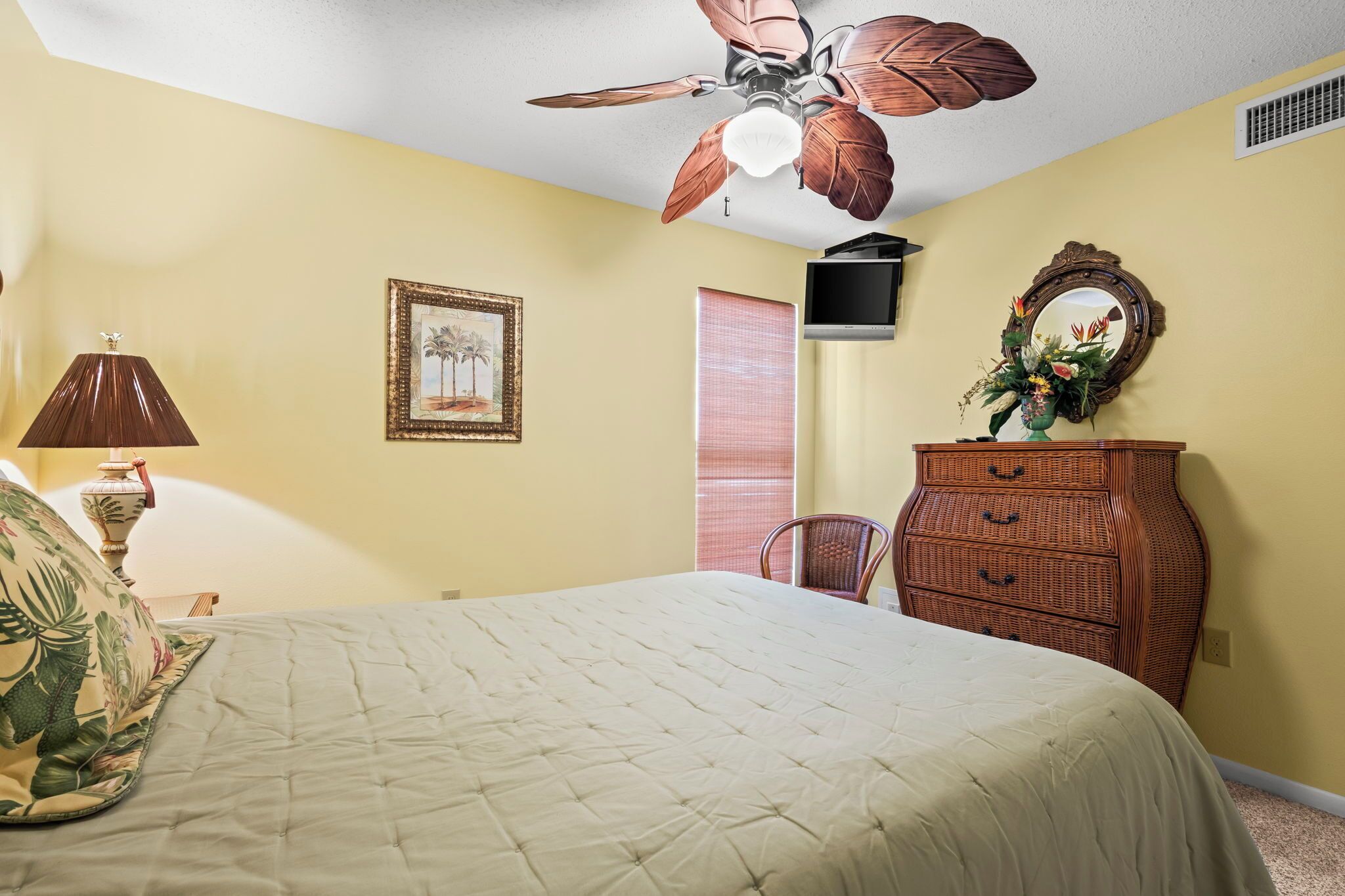 A bedroom with a bed, a ceiling fan, a dresser, a television, a framed picture, and a window with blinds.