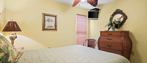 A bedroom with a bed, a ceiling fan, a dresser, a television, a framed picture, and a window with blinds.