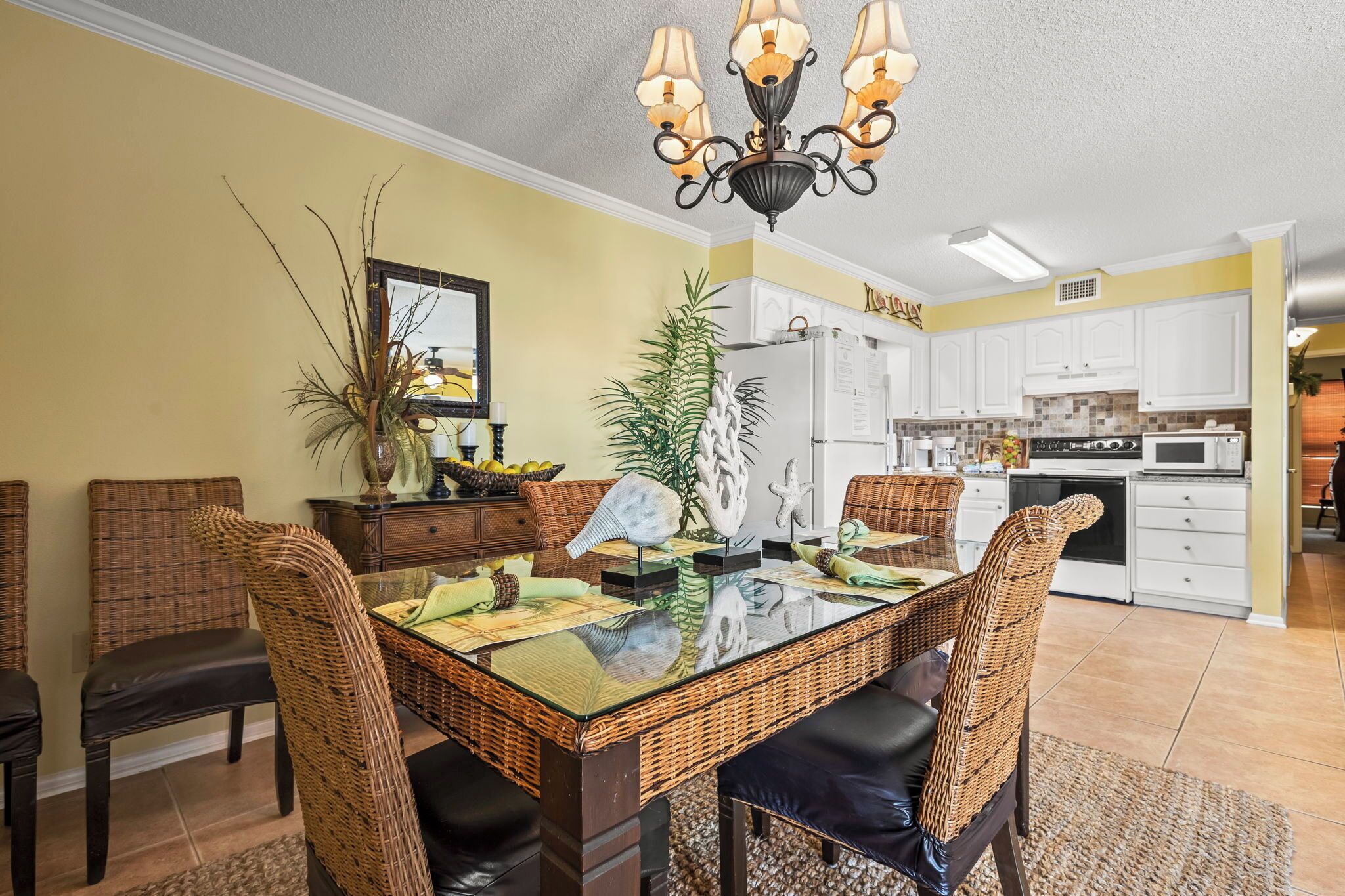 A dining area with a glass-top table, wicker chairs, and a chandelier.