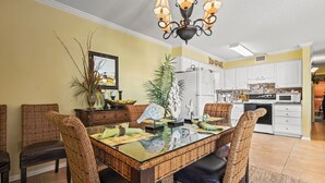 A dining area with a glass-top table, wicker chairs, and a chandelier. - Family fun in this beautiful, beachside condo (Gulf Shores)