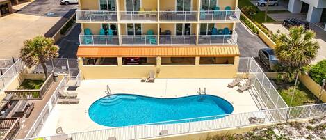 Un hotel de varios pisos con piscina en la planta baja, asientos al aire libre y vistas del entorno.