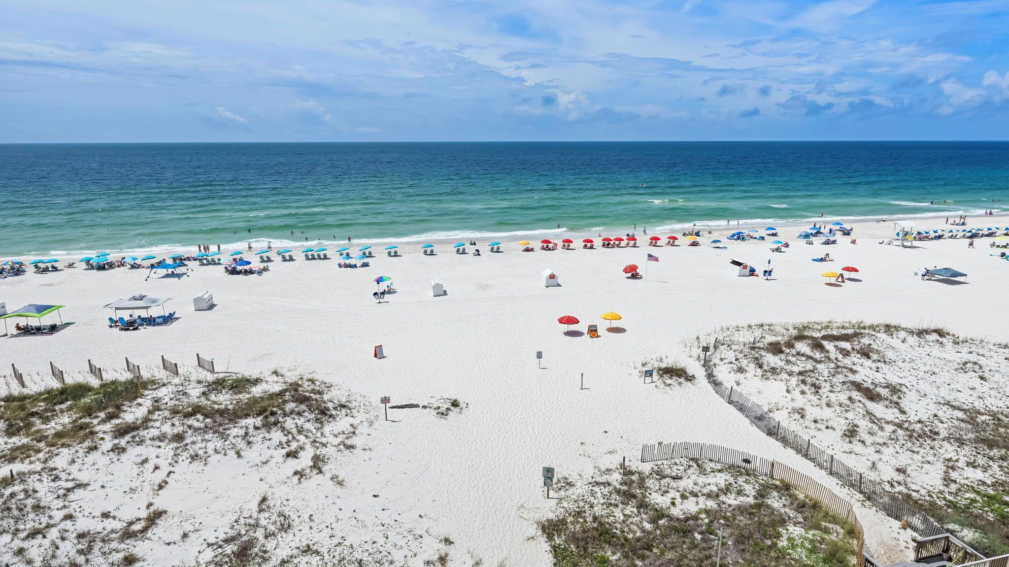 A beach with white sand, clear blue water, and numerous umbrellas.