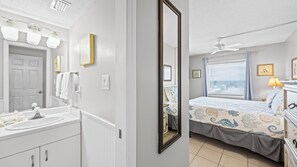 Une chambre à coucher comprenant un lit, une table de chevet, une fenêtre avec des stores et un ventilateur de plafond.