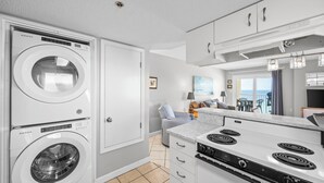 A compact kitchen with a washing machine, a stove, and a dining area with a view.