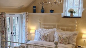 A bedroom with a four-poster bed, a chandelier, a window with shutters, and a bedside table with a lamp. - Romantic Cottage, Perranporth, Sleeps 2, Dog friendly, Walking distance to Beach (Perranporth)