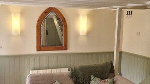 Ein beiges Sofa mit floralen Kissen, ein Holztisch, ein Spiegel mit Holzrahmen und Wandleuchten.