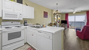 Une cuisine avec des armoires blanches, un four à micro-ondes, une cuisinière et un lave-vaisselle. On y trouve également un coin repas avec une chaise rouge et une table.