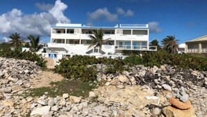 Un edificio bianco a più piani con balconi, immerso in un paesaggio roccioso e palme.