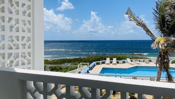 Un balcone con vista su una piscina, palme e un cielo azzurro limpido.