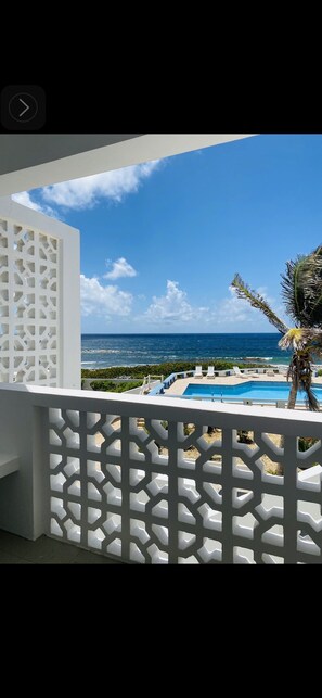 A balcony with a view of a swimming pool, palm trees, and a clear blue sky.