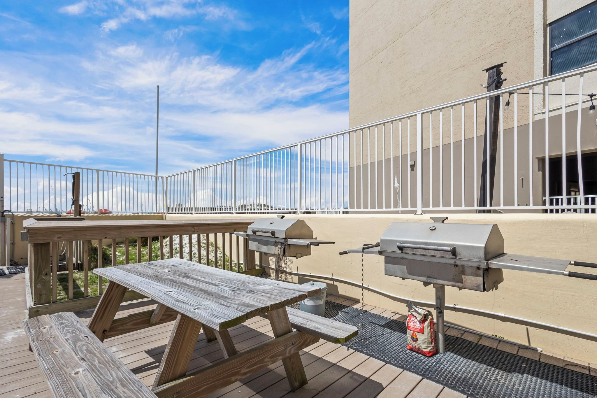 An outdoor patio with a wooden table and barbecue grills.