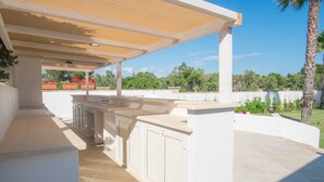 Una zona de cocina al aire libre con una pérgola, armarios empotrados y una encimera de piedra.