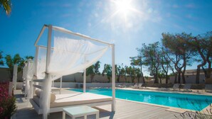Zona junto a la piscina con un toldo blanco, sillones de descanso y una piscina.