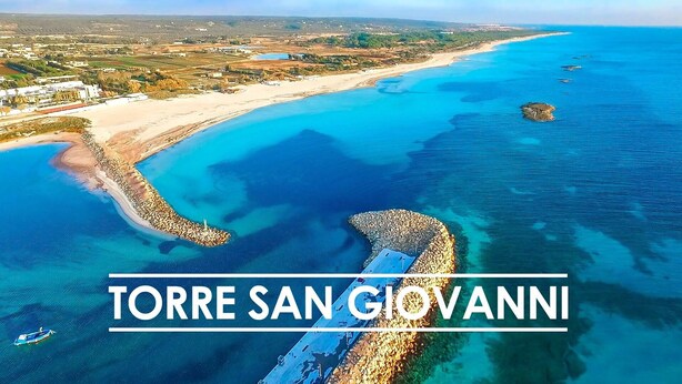 Vista aérea de Torre San Giovanni con aguas azul turquesa, una playa de arena y un litoral rocoso.