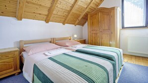 Ein Schlafzimmer mit Holzboden, einem Doppelbett mit gestreifter Bettwäsche, einem Nachttisch, einem Kleiderschrank und einem Fenster mit Vorhängen.