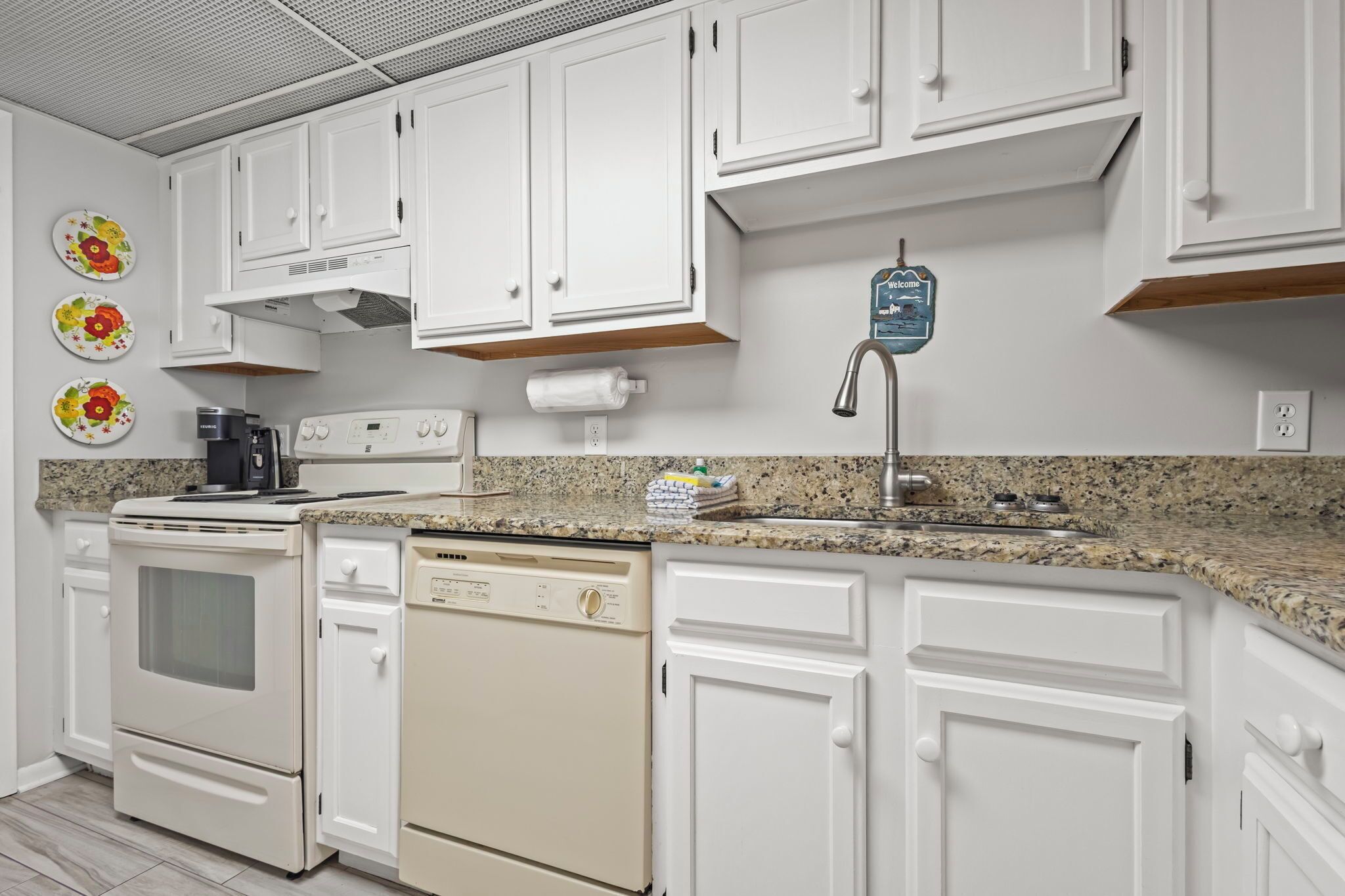 A kitchen with white cabinets, a granite countertop, a coffee maker, a dishwasher, and a water dispenser.
