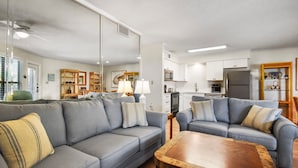A modern living room with a grey sofa, wooden coffee table, and a kitchen in the background. - Great family beachview condo ~ Low-rise complex (Gulf Shores)
