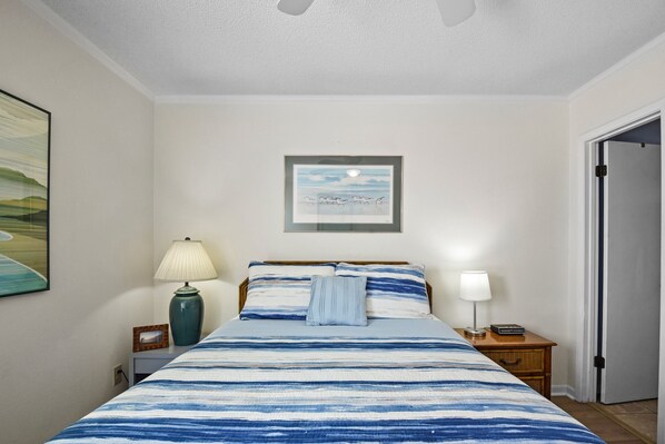 A neatly arranged bedroom with a bed, two bedside tables, a nightstand, a framed picture on the wall, and a door to the right.