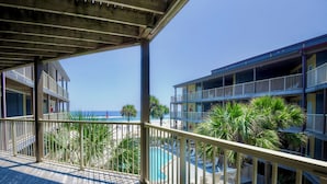 A wooden deck with a pool and palm trees, overlooking a beach and a multi-story building with balconies. - Great family beachview condo ~ Low-rise complex (Gulf Shores)