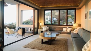 A spacious living room with a large window, a ceiling fan, and a round coffee table. - 5 Star Luxe, Ocean Views, Walk to Beach & Village, Full Staff, 8-10 BR Rates (Sayulita)