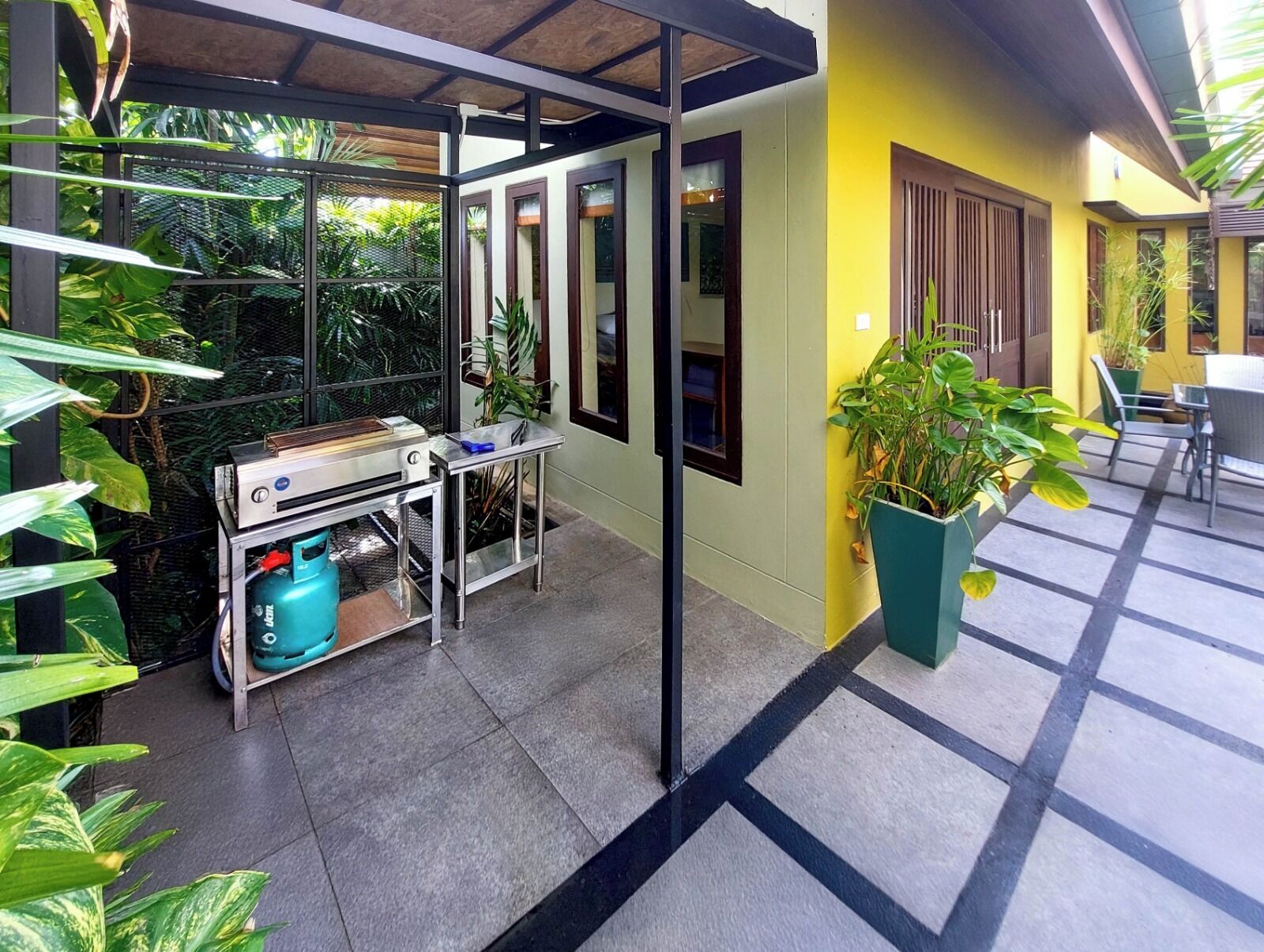 An outdoor patio area with a grill, seating, and potted plants.