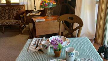 A dining area with a table set for two, featuring floral tableware and a vase with purple flowers.