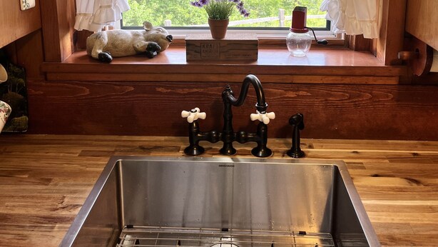A kitchen with a stainless steel sink, wooden countertop, and a window with white curtains.