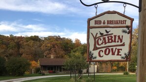 A sign for Cabin Cove Bed & Breakfast with a rustic wooden signboard, a lawn, and a building in the background.
