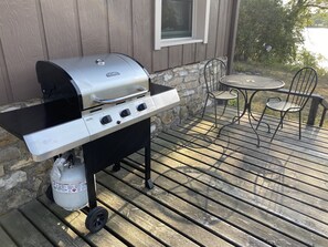 A stainless steel grill with a gas tank, a table, and two chairs on a wooden deck. - Cabin Cove on the river (Iowa Falls)
