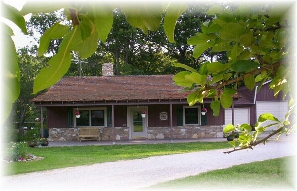 A rustic building with a stone foundation and a wooden roof, featuring a bench and hanging flower baskets. - Cabin Cove on the river (Iowa Falls)