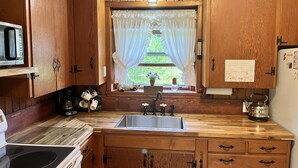 A kitchen with wooden cabinets, a stainless steel sink, a stove, and a window with curtains.