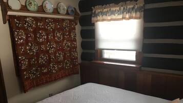 A bedroom with a bed, a quilt, a window with blinds, and a wall with a striped pattern.