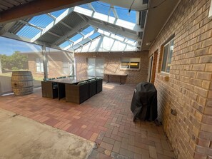 Une terrasse extérieure avec une longue table, un barbecue et un espace salon abrité.
