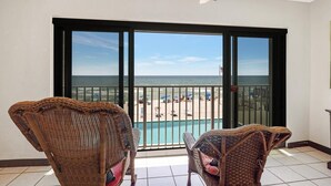 Un balcón con sillones de mimbre, vista a una playa y una piscina.