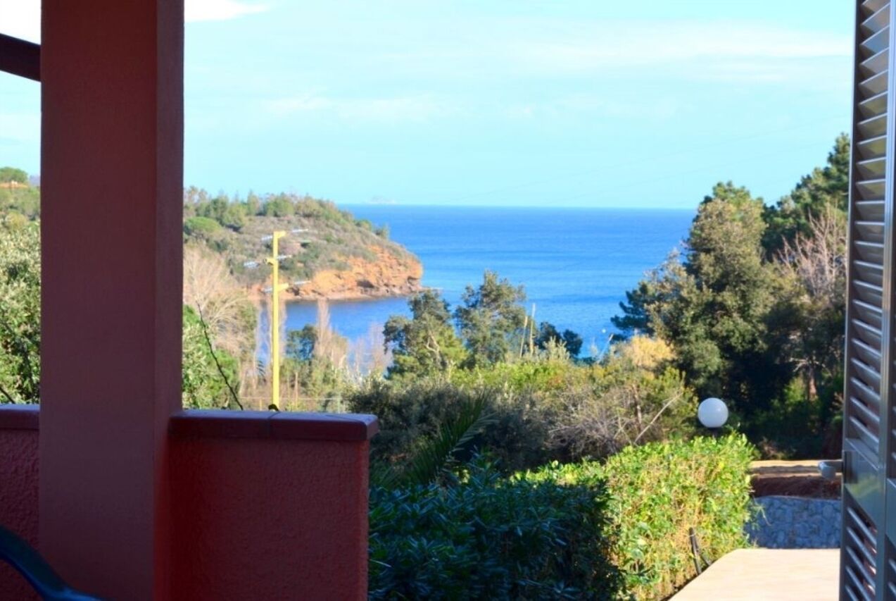 A coastal view from a balcony with a clear sky, a rocky shoreline, and dense greenery.