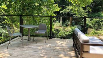 A wooden deck with a table and chairs, surrounded by lush greenery.