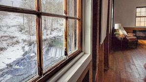 Ein Zimmer mit großem Fenster, Holzboden und einem kleinen Tisch mit Lampe.